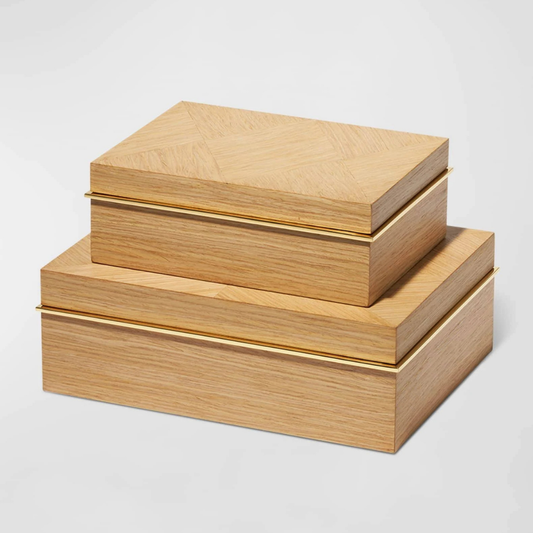 Two Marcello Box Oak by Aerin, crafted from European oak with gold hinges, are stacked atop each other. Their light wood finish and sleek lines make them elegant decorative desk organizers against a plain white background.