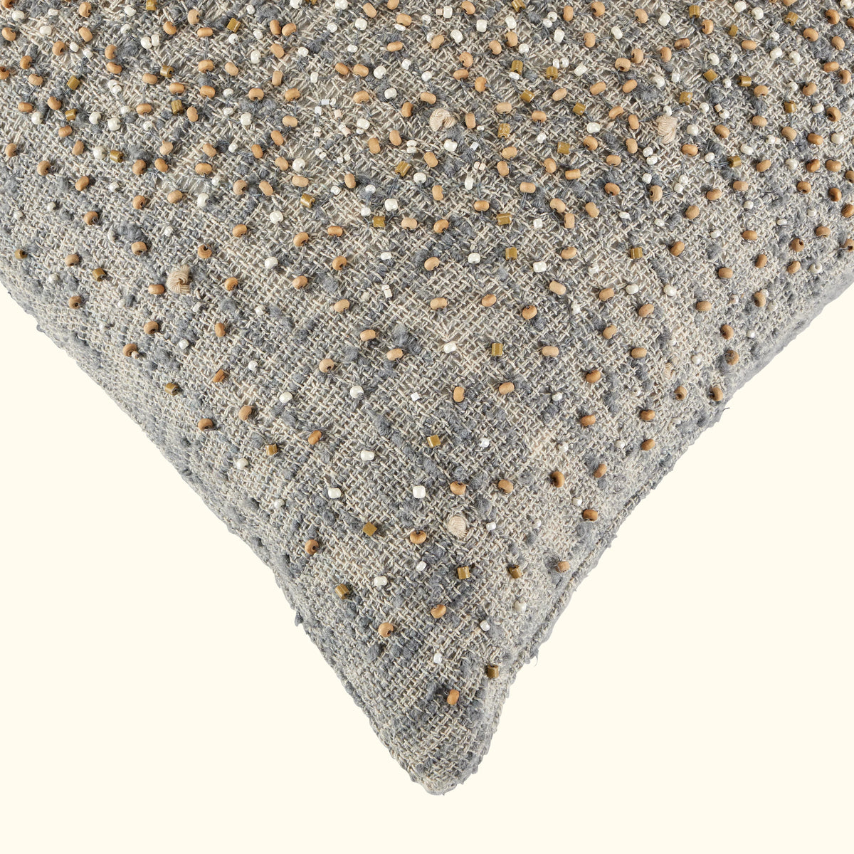 Close-up of the Bead Burst Pillow Azure 22 x 22 by Threads Soft Goods, highlighting artisanal craftsmanship with grey textured jacquard fabric and scattered beige and brown beads on an off-white background.