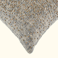 Close-up of the Bead Burst Pillow Azure 22 x 22 by Threads Soft Goods, highlighting artisanal craftsmanship with grey textured jacquard fabric and scattered beige and brown beads on an off-white background.
