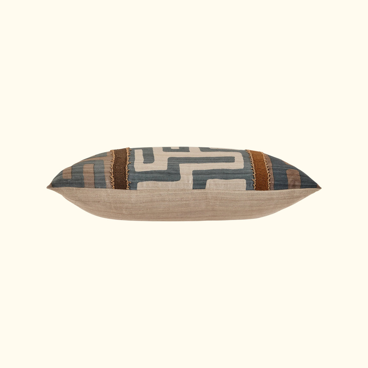 The Kasai Pillow 16 x 24 by Threads Soft Goods features a handcrafted geometric Kuba cloth design in muted blue, beige, and brown. Shown with a plain light background, this rectangular pillow adds decorative flair to any space.