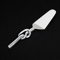 The Inspired Generations Knotty Cake Server features a modern stainless steel design with a shiny silver looped handle, shown against a black background.