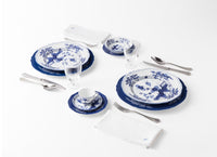 Two place settings of Ginori 1735 Oriente Italiano Indaco porcelain, featuring floral patterned plates, bowls, and a small teacup, accompanied by silverware, glassware, and folded white napkins.