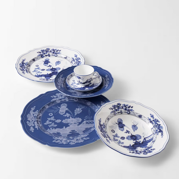 A set of Ginori 1735 Oriente Italiano Indaco porcelain dinnerware in blue and white, featuring scalloped edges and intricate floral and landscape patterns.