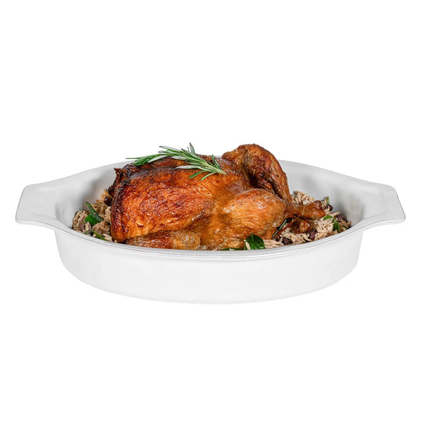 Savor a roast chicken garnished with rosemary, presented on a bed of rice in the Juliska Puro Oval Baker Whitewash 16″—an elegant piece of Portuguese stoneware designed for seamless oven-to-table serving.