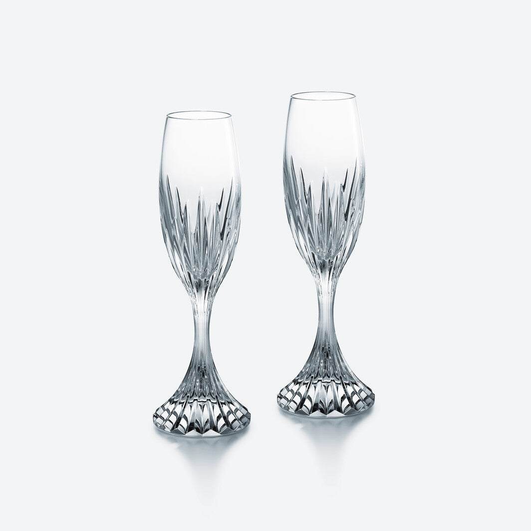 Two clear, intricately cut crystal flutes from the Massena Flutes, Set of 2 by Baccarat, with flared, textured bases stand side by side on a plain, light background—a stunning example of luxury crystal glassware.