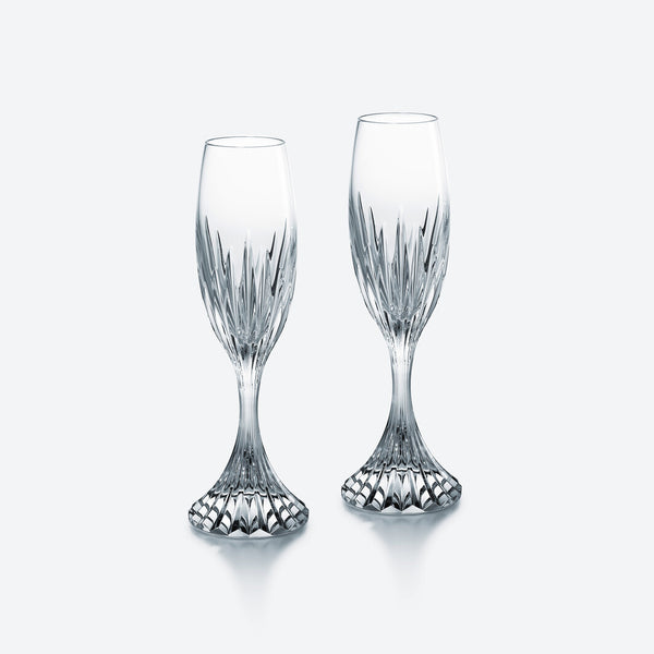 Two clear, intricately cut crystal flutes from the Massena Flutes, Set of 2 by Baccarat, with flared, textured bases stand side by side on a plain, light background—a stunning example of luxury crystal glassware.