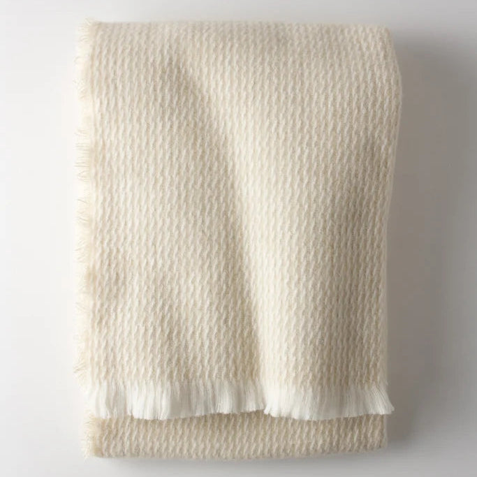 The Four Sided Pinstripe Fringe Throw by A Soft Idea, a folded cream wool blend with subtle fringe, adds a cozy blanket touch to any space.