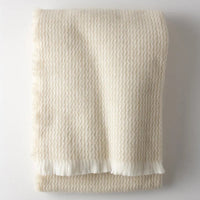 The Four Sided Pinstripe Fringe Throw by A Soft Idea, a folded cream wool blend with subtle fringe, adds a cozy blanket touch to any space.