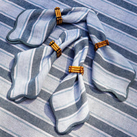 Four Juliska Cabana Stripe Napkins in Ocean (set of 4) are arranged on a matching tablecloth, each paired with bamboo napkin rings.