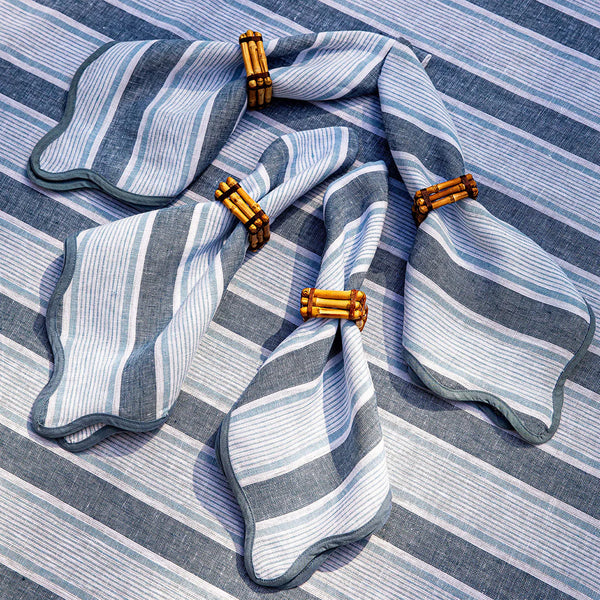 Four Juliska Cabana Stripe Napkins in Ocean (set of 4) are arranged on a matching tablecloth, each paired with bamboo napkin rings.