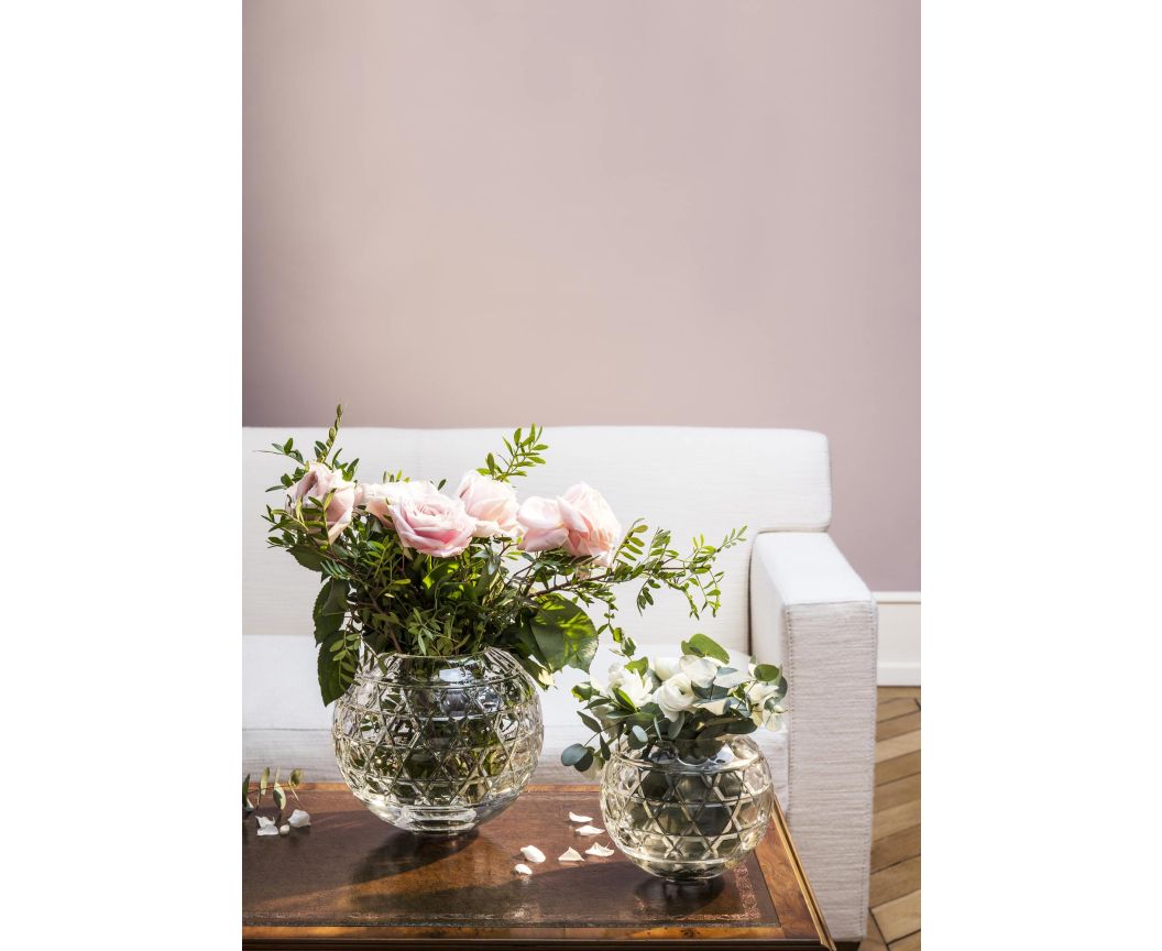 Two round, faceted Royal Vase - Saint-Louis/Hermes crystal vases holding bouquets of flowers on a wooden table in front of a sofa.