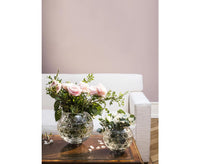 Two round, faceted Royal Vase - Saint-Louis/Hermes crystal vases holding bouquets of flowers on a wooden table in front of a sofa.
