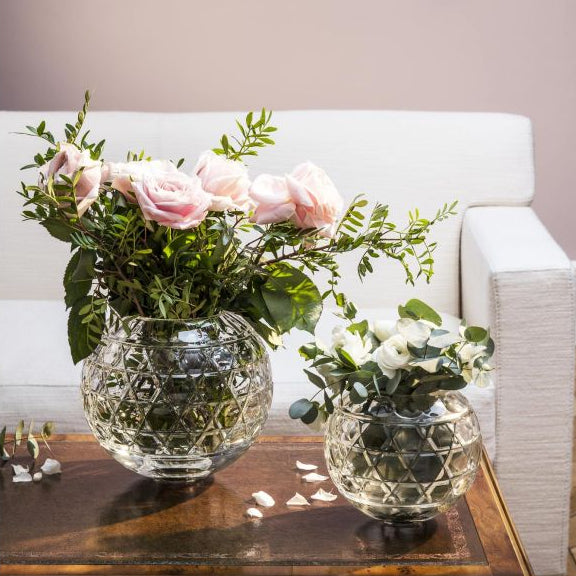 Two Saint-Louis Royal Vase crystal vases with a geometric faceted pattern, each holding a bouquet of pink roses and white flowers, sitting on a wooden table.