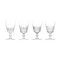 A set of four Queen’s Hall glasses by Saint-Louis/Hermès, each featuring a distinct etched or cut pattern on the bowl and a short, rounded pedestal base, displayed in a row against a white background—capturing the timeless elegance of tableware once found in the Palace of Versailles.