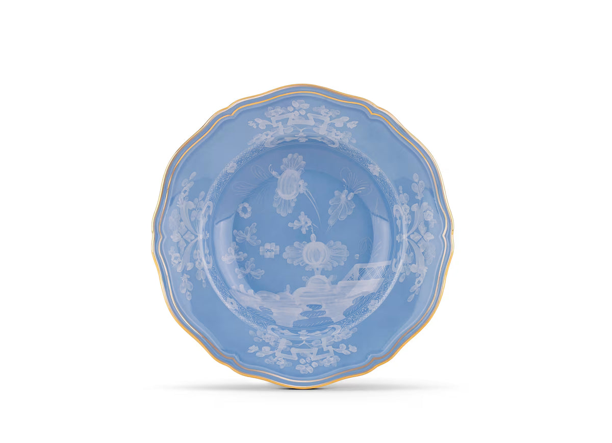 An Oriente Italiano Pervinca dinner plate by Ginori 1735, featuring scalloped edges, 24-karat gold trim, and intricate white floral and landscape designs on blue porcelain, displayed against a white background.
