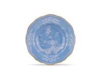 An Oriente Italiano Pervinca dinner plate by Ginori 1735, featuring scalloped edges, 24-karat gold trim, and intricate white floral and landscape designs on blue porcelain, displayed against a white background.