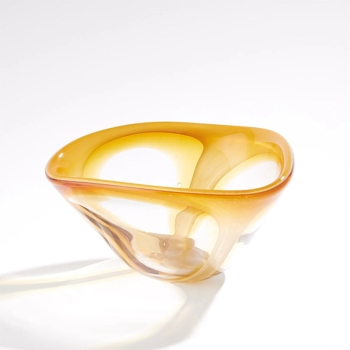 The Enigma Bowl – Amber by Global Views / Surya features organic, smooth, and asymmetrical curves in art glass. Set against a plain white background, light reflections accentuate its translucent, glossy surface, making this piece a striking decorative catchall.