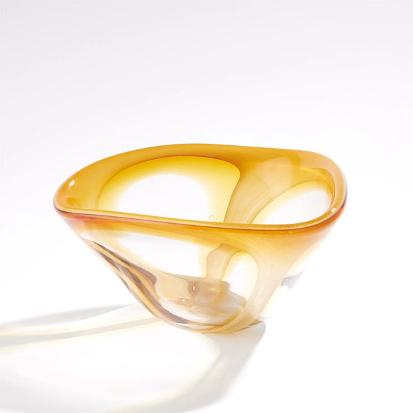 The Enigma Bowl – Amber by Global Views / Surya features organic, smooth, and asymmetrical curves in art glass. Set against a plain white background, light reflections accentuate its translucent, glossy surface, making this piece a striking decorative catchall.