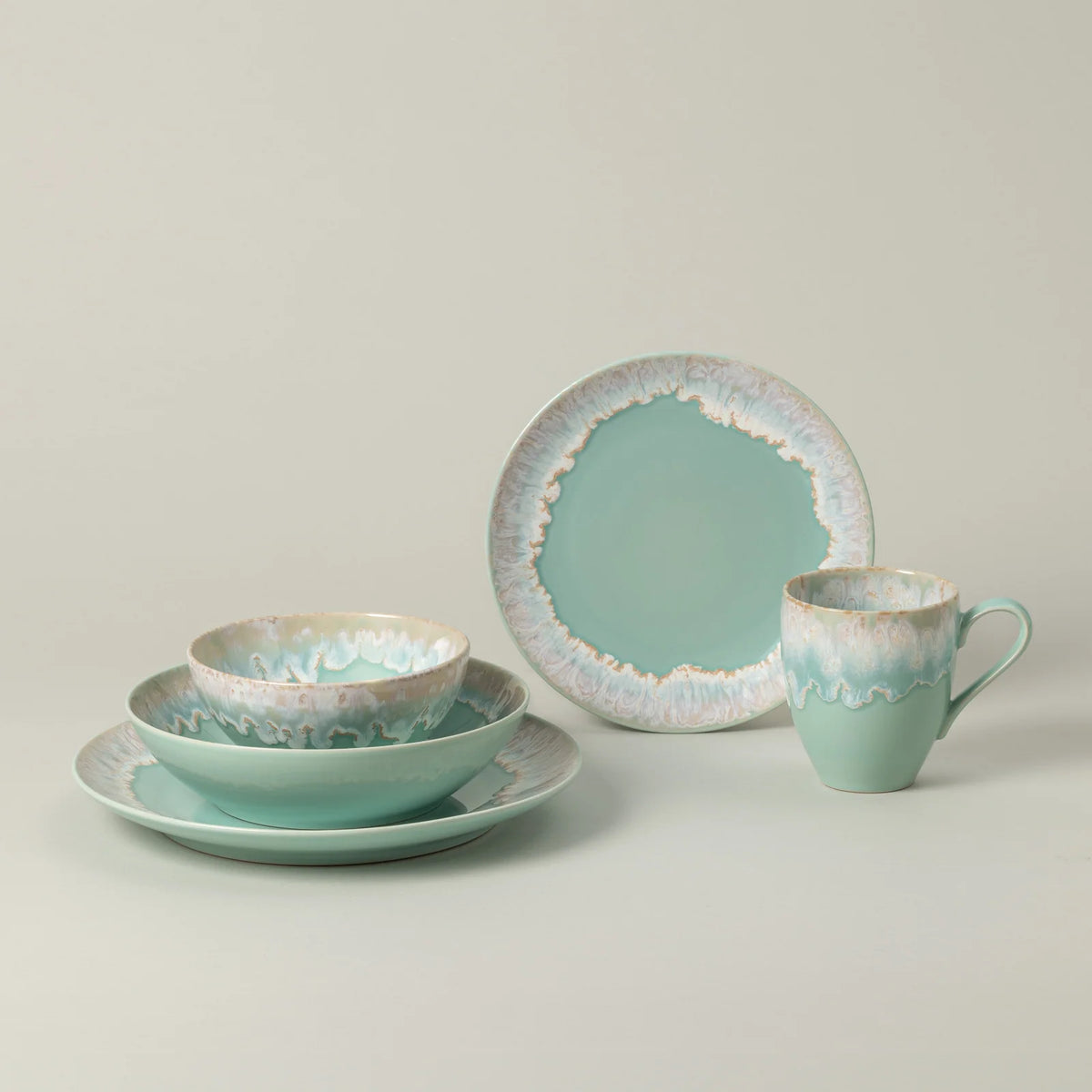 Taormina Aqua Dinnerware set in aqua ceramic, including a dinner plate, a shallow bowl, a smaller bowl, and a mug, all featuring an irregular, textured white and brown rim.