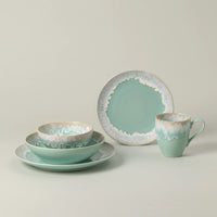 Taormina Aqua Dinnerware set in aqua ceramic, including a dinner plate, a shallow bowl, a smaller bowl, and a mug, all featuring an irregular, textured white and brown rim.
