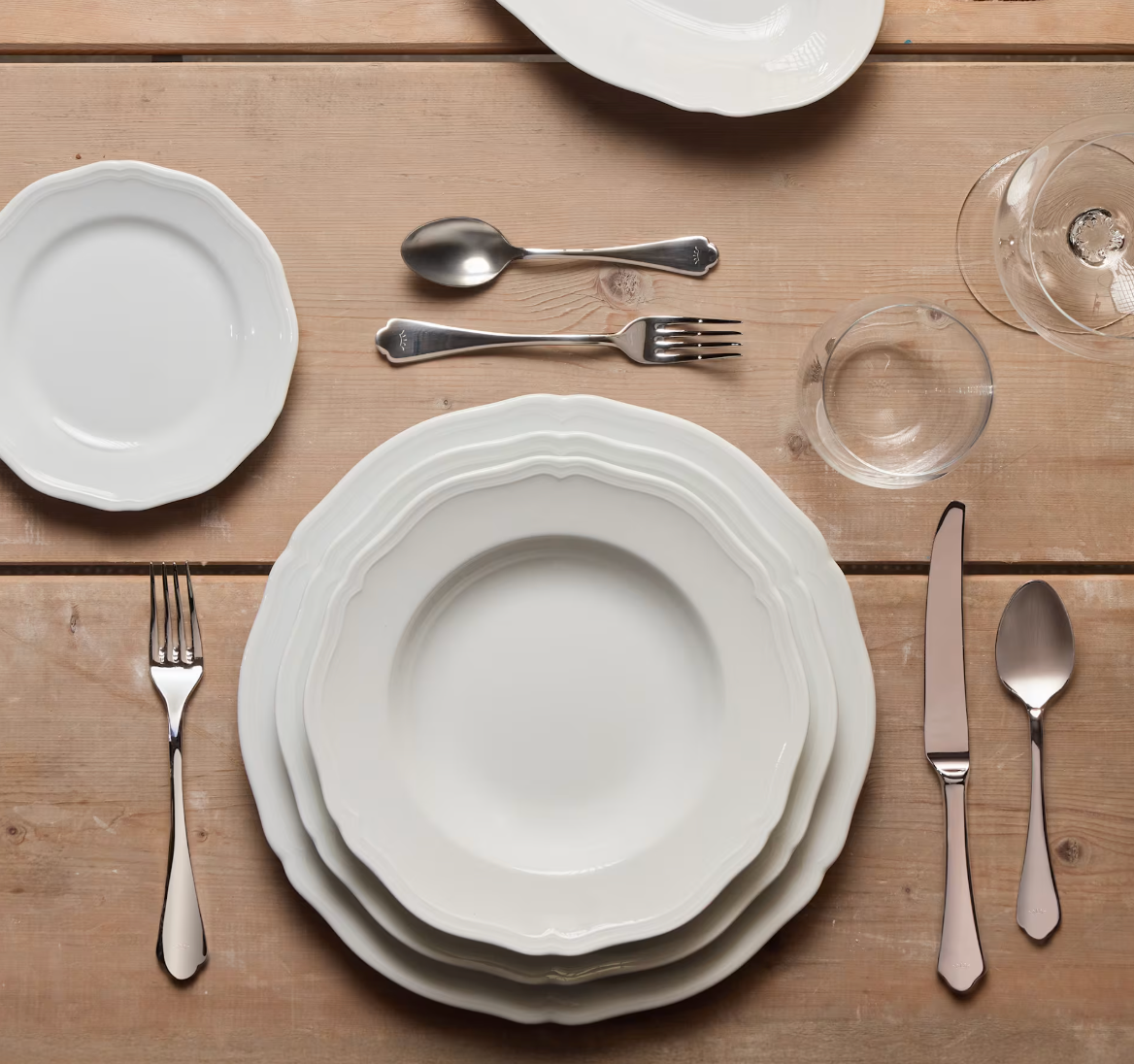 A formal table setting featuring Ginori 1735’s Antico Doccia Dinnerware, complemented by elegant silverware, a glass, and a wine glass arranged neatly on a wooden table, creates an atmosphere of timeless design.