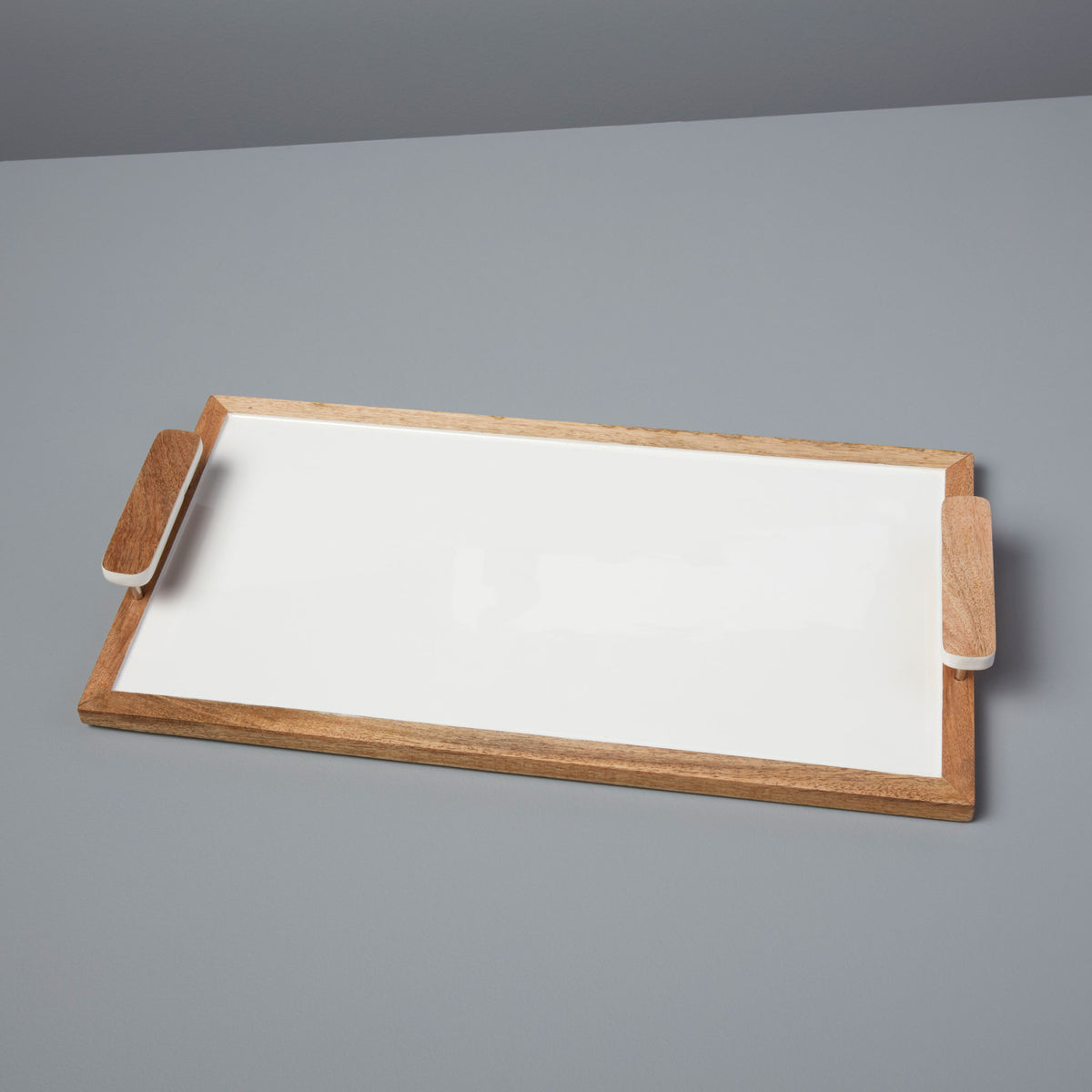 The Be Home Mayan Wood Handled Rectangle Tray, handcrafted from sustainably sourced materials, features a white surface, wooden frame, and dual wood handles on each side, shown on a light gray background.