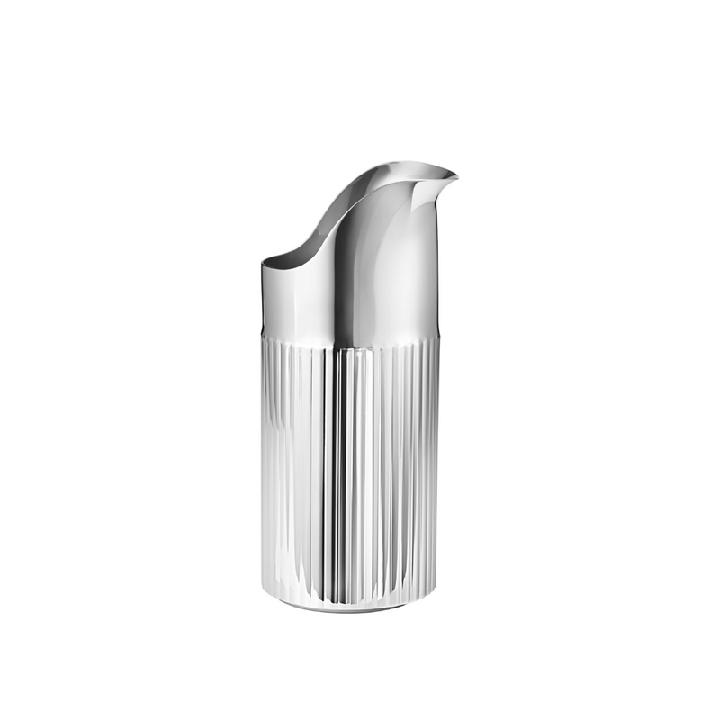 The Georg Jensen Bernadotte Stainless Creamer features a sleek, modern design with ribbed texture on the lower half, smooth upper, curved spout, and a reflective stainless steel finish, shown against a white background.