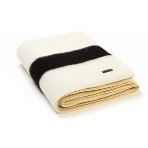 The Siempre Recycled Alpaca Throw by Blacksaw is a folded cream heavyweight blanket with a bold black stripe, beige ribbed edges, and visible label—ideal as a cozy fireside companion. Shown on a white background.