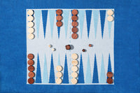 The G. McGee Southampton Beach Backgammon set features light and dark wooden pieces, three dice showing 2, 3, and 1, on a blue and white board next to a plush cotton terry luxury beach towel.