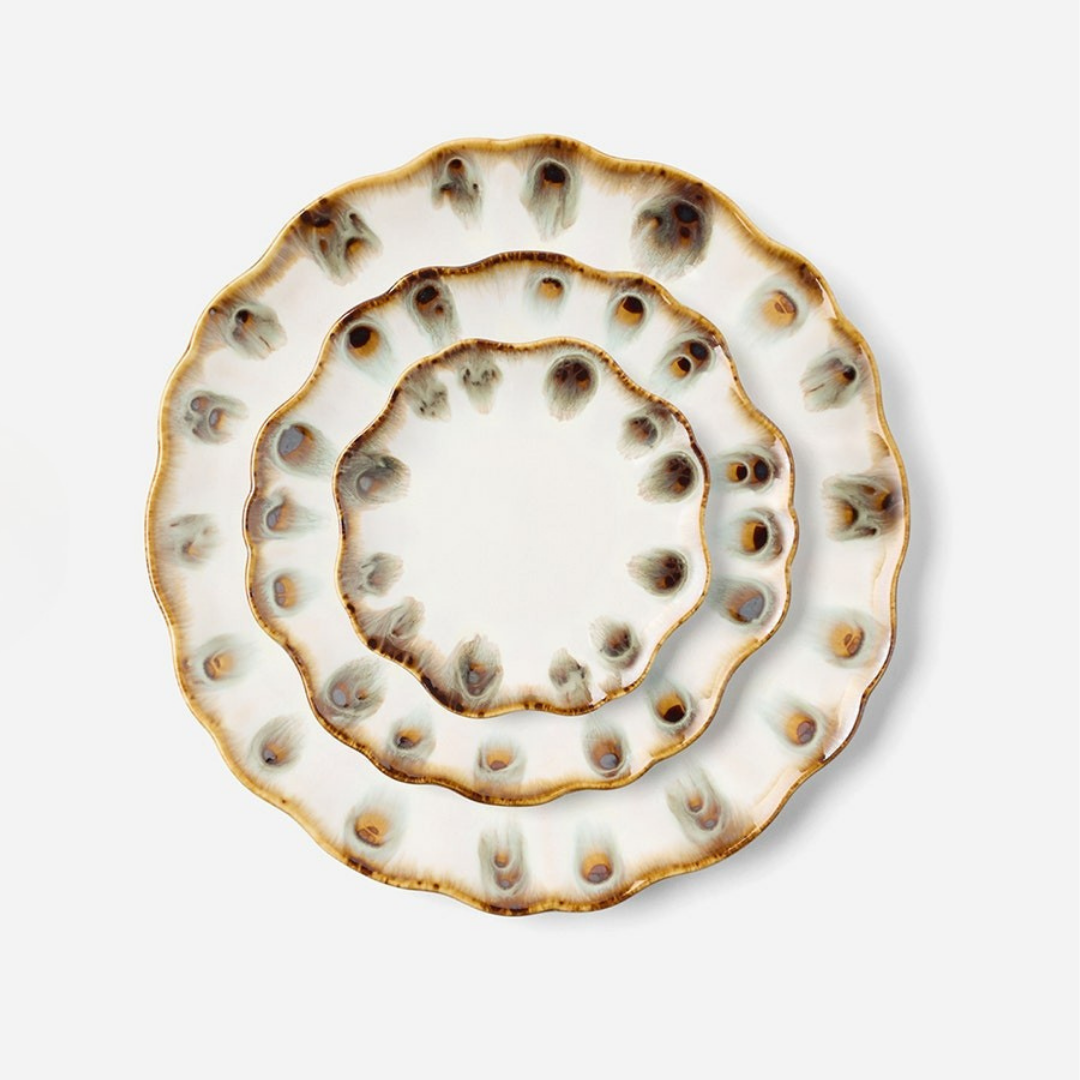 Three scalloped ceramic plates from Blue Pheasant’s Amoria Dinnerware collection, featuring a white base and brown, blue, and beige speckled edges, are stacked concentrically on a plain light background—these pieces of scalloped edge serveware showcase vintage-inspired elegance enhanced by a subtle reactive glaze.