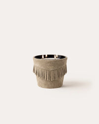 A Baobab Calamity Jane Candle - The Plains, featuring three wicks in a mineral taupe leather, light brown fringed container with a single flame lit.