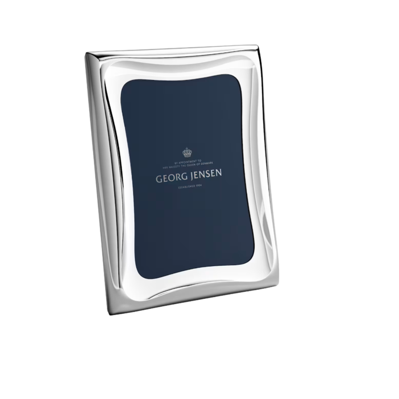 The Cobra Stainless Picture Frame by Georg Jensen is a shiny silver rectangular frame with wavy edges, standing upright and featuring a dark blue placeholder with the brand’s logo and text.