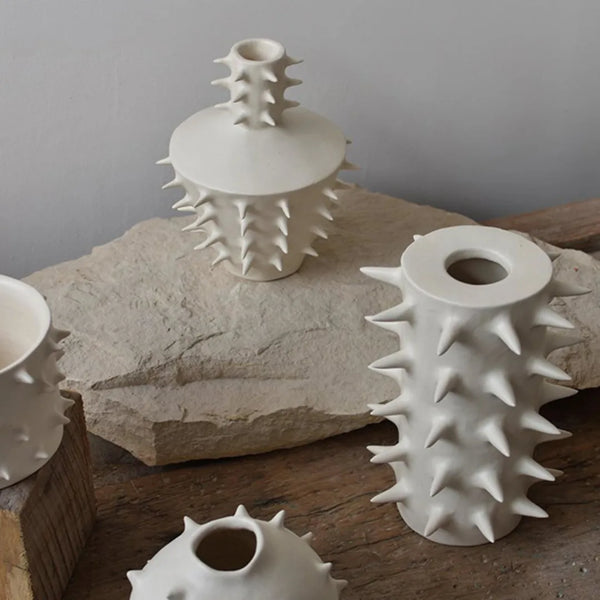 Three “Spikes Vase III - White” vases by OWO Ceramics, each featuring striking sculptural spikes, are displayed on rustic stone and wood surfaces against a simple gray background, creating truly unique home decor.
