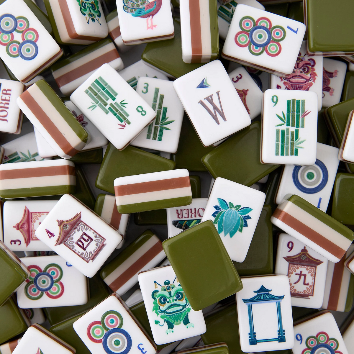 A pile of Mahjong tiles with green backs, showcasing colorful designs, numbers, letters, Chinese characters, flowers, dragons, and bamboo. These luxury game tiles from Oh My Mahjong’s Mahjong Tiles Set – Drake are crafted from high-quality acrylic and are arranged in an overlapping random pattern.