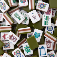 A pile of Mahjong tiles with green backs, showcasing colorful designs, numbers, letters, Chinese characters, flowers, dragons, and bamboo. These luxury game tiles from Oh My Mahjong’s Mahjong Tiles Set – Drake are crafted from high-quality acrylic and are arranged in an overlapping random pattern.