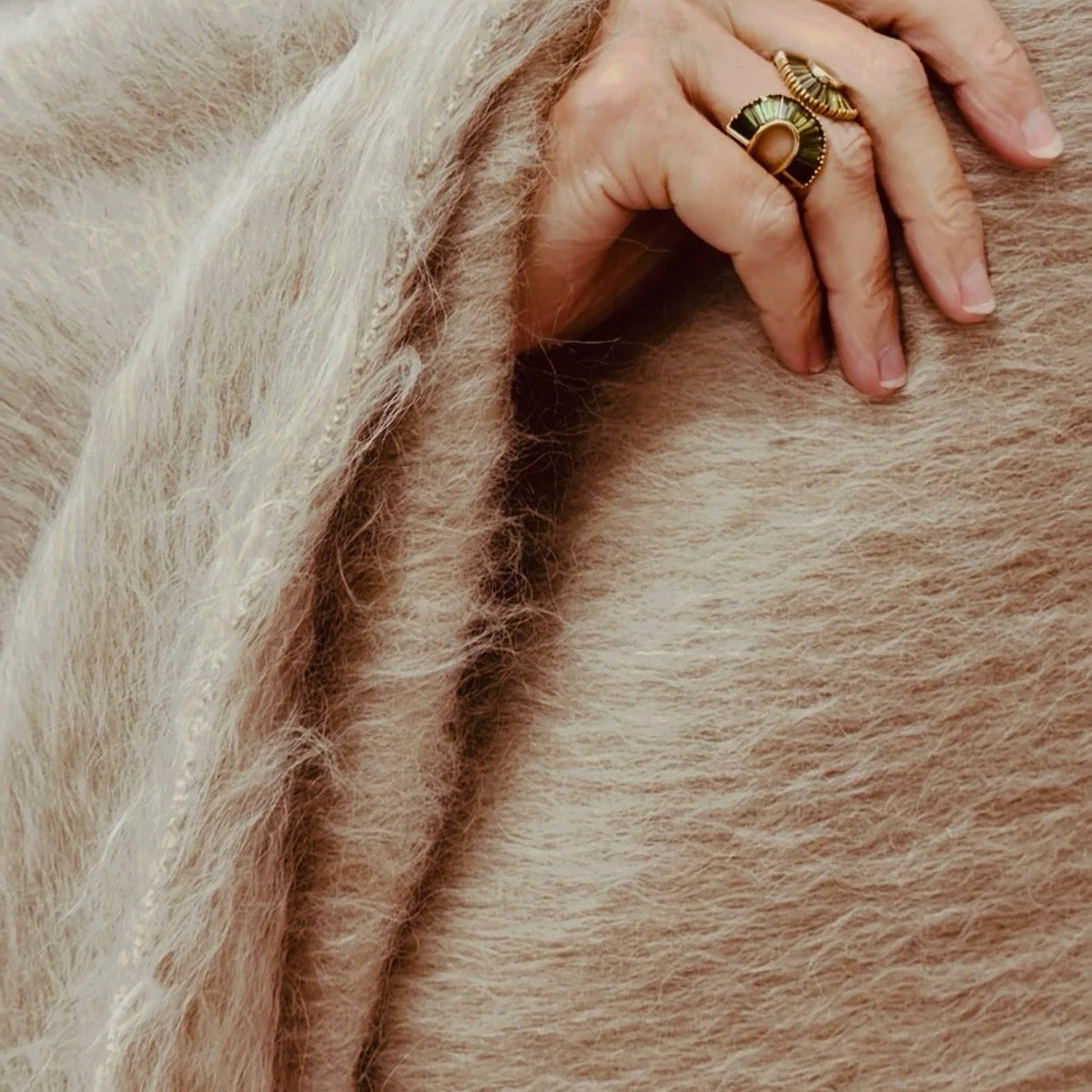A hand with two gold rings resting on a fuzzy, tan-colored Dove & Donkey Woolly Mammoth Throw.