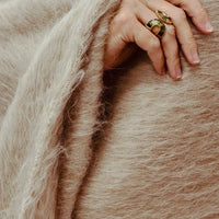 A hand with two gold rings resting on a fuzzy, tan-colored Dove & Donkey Woolly Mammoth Throw.
