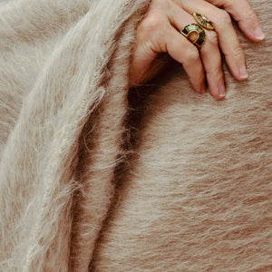 A hand with two gold rings resting on a fuzzy, tan-colored Dove & Donkey Woolly Mammoth Throw.