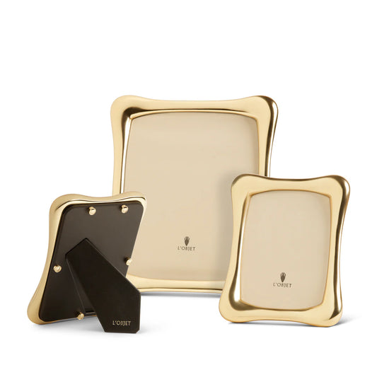 Three elegant Anton Frame Gold photo frames by L'Objet in varying sizes are displayed; two highlight the gold front with logo, and one is turned to show the black stand and back—an impressive luxury frame set.