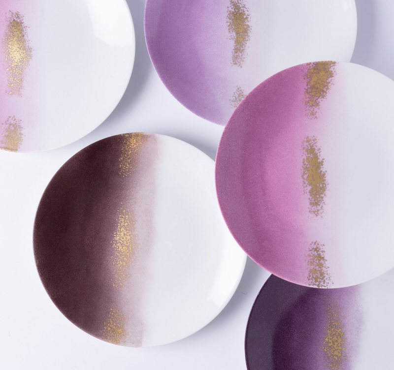Five Marie Daâge Horizon Gold Dinnerware plates overlap on a white background, showcasing hand-painted gradients in white, purple, and gold tones with gold speckles. This signature Marie Daâge tableware features striking color depth.