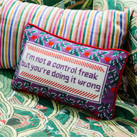 The Furbish Needlepoint Pillow - Control Freak features colorful embroidery that reads, "I'm not a control freak but you're doing it wrong," with floral patterns, shown on patterned fabric next to a striped pillow.