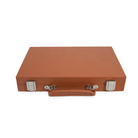 The Mini Travel Backgammon Set by Brouk & Co is a closed rectangular brown leather case with a handle and two silver clasps, resembling a portable backgammon game, shown against a white background.
