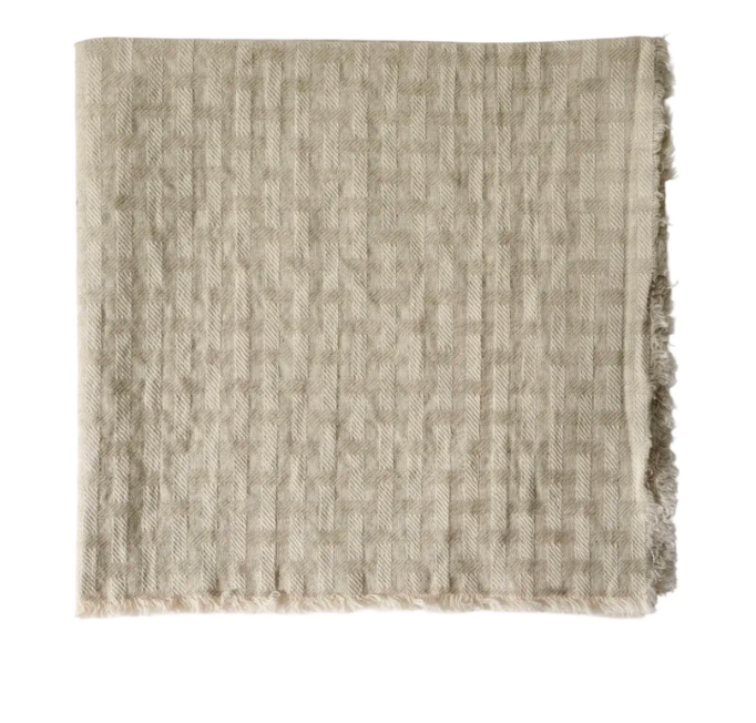 A set of four beige, textured fabric napkins by Deborah Rhodes, featuring a subtle checkered pattern and slightly frayed edges inspired by the Lattice Fringe Napkin collection.