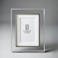 The Prisma Frame Lip - Grey by Bella Moulding is a clear acrylic photo frame with a silver inset and white mat, crafted from archival materials. The frame features the Current Home logo on the white mat.