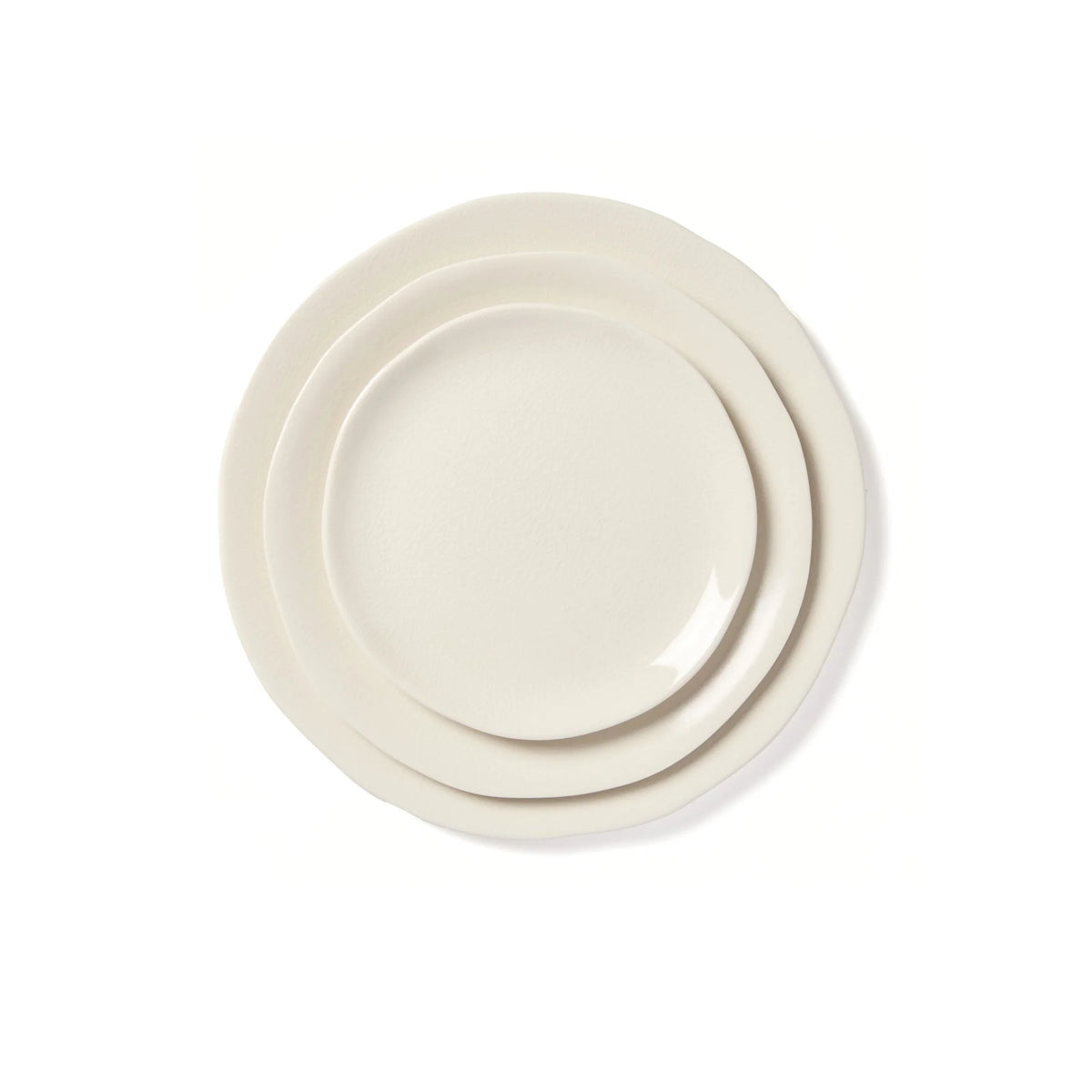 Three off-white ceramic plates from the Maguelone Dinnerware Quartz collection by Jars - Rosenthal, each a different size, are stacked together on a white background. Every plate features an irregular, organic-shaped edge, beautifully reminiscent of Mediterranean dinnerware.