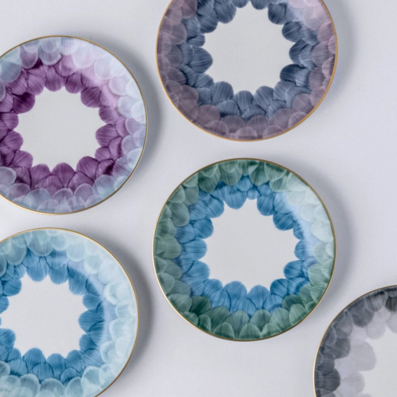 Five Marie Daâge Cercle D'Ecailles Gold Filet plates by Marie Daâge, featuring petal-like scalloped designs in purple, blue, and green with gold rims and white centers, arranged on a light background.
