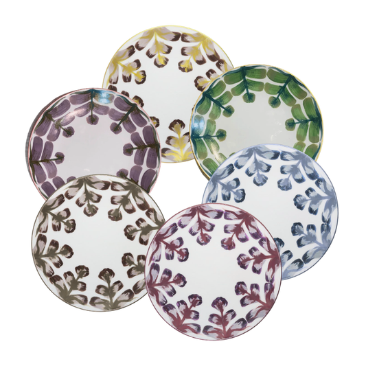 Six round ceramic plates from Marie Daâge’s Marqueyssac 1 collection, each with a colorful leaf design on white, evoke the look of hand-painted French tableware.