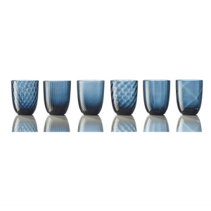 The Nason Moretti Idra Mixed Pattern Glass Set of 6 showcases blue glass tumblers, each with a unique texture, inspired by Murano artistry and arranged on a reflective surface with a white background.