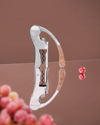 L’ Atelier du Vin Lever Wine Opener - Silver with a wooden handle, reflecting on a polished surface next to two grapes.