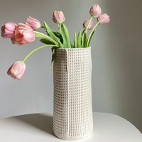A cream-colored Pixel Cylinder Vase Cream by CYM Warkov Ceramics with a grid-textured pattern, holding a bouquet of pink tulips.